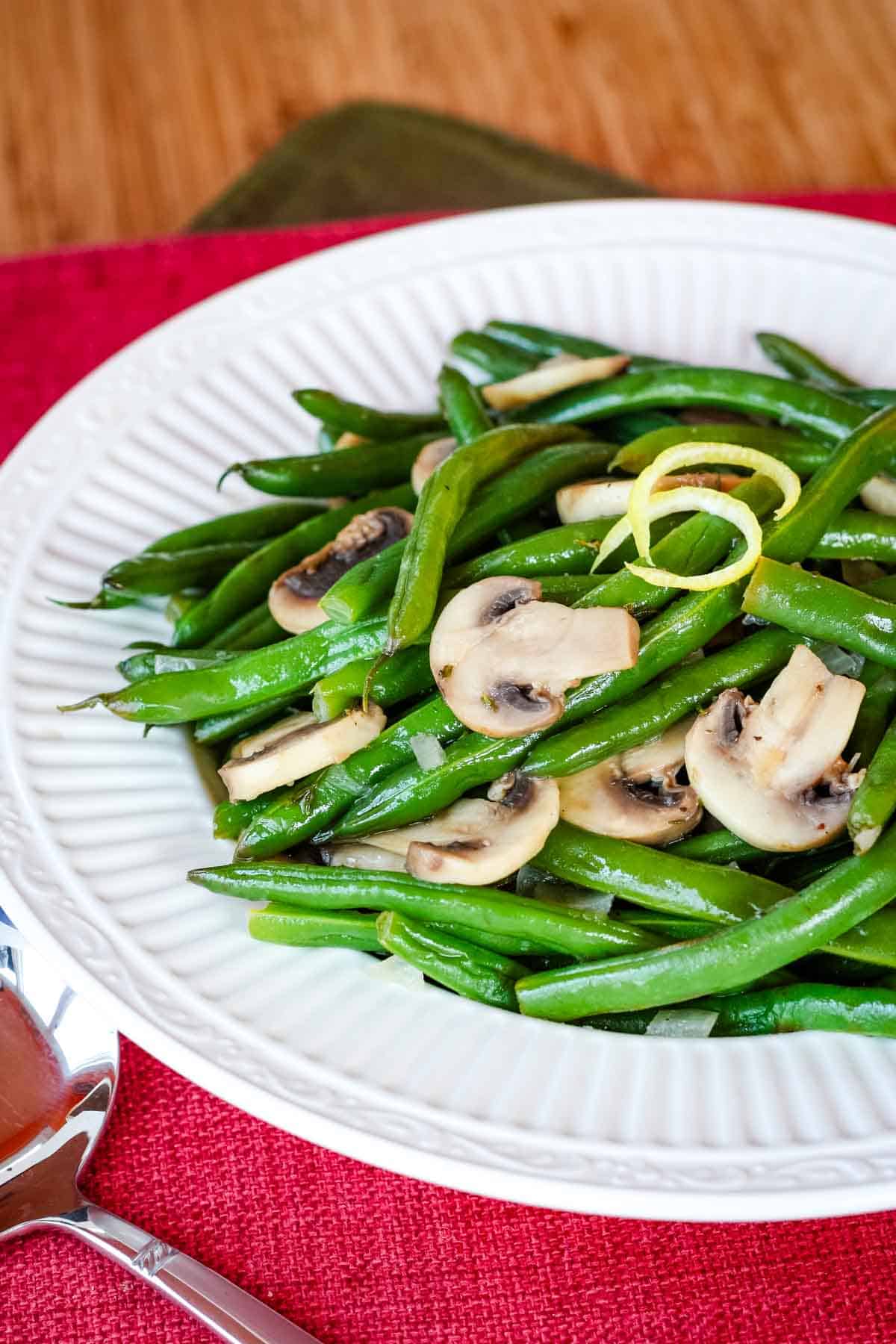 A white plate of green beans and mushrooms on a red napkin.