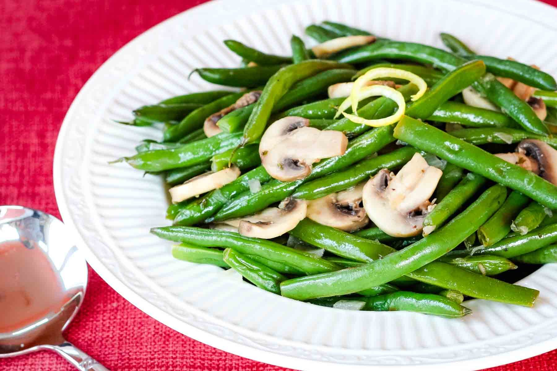 Sliced mushrooms and lemony green beans on a white plate.