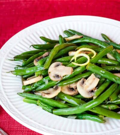 Sliced mushrooms and lemony green beans on a white plate.