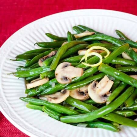 Sliced mushrooms and lemony green beans on a white plate.