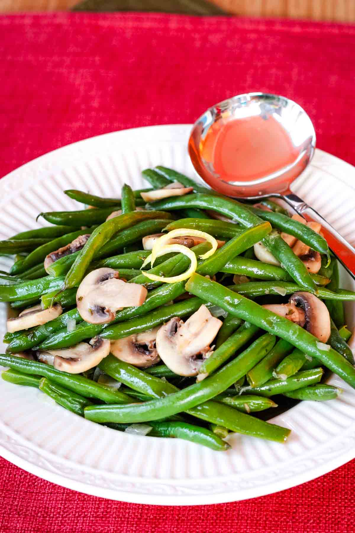 A plate of green beans and mushrooms on a red background.