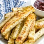 Crispy French fries flecked with herbs on a plate with text overlay that says "Oven-Baked Italian Fries".