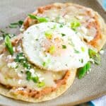 A plate of breakfast tostadas is topped with fried eggs and garnished with cilantro.
