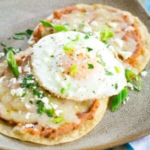 A plate of breakfast tostadas is topped with fried eggs and garnished with cilantro.