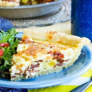 A slice of bacon cheddar quiche with salad on a plate