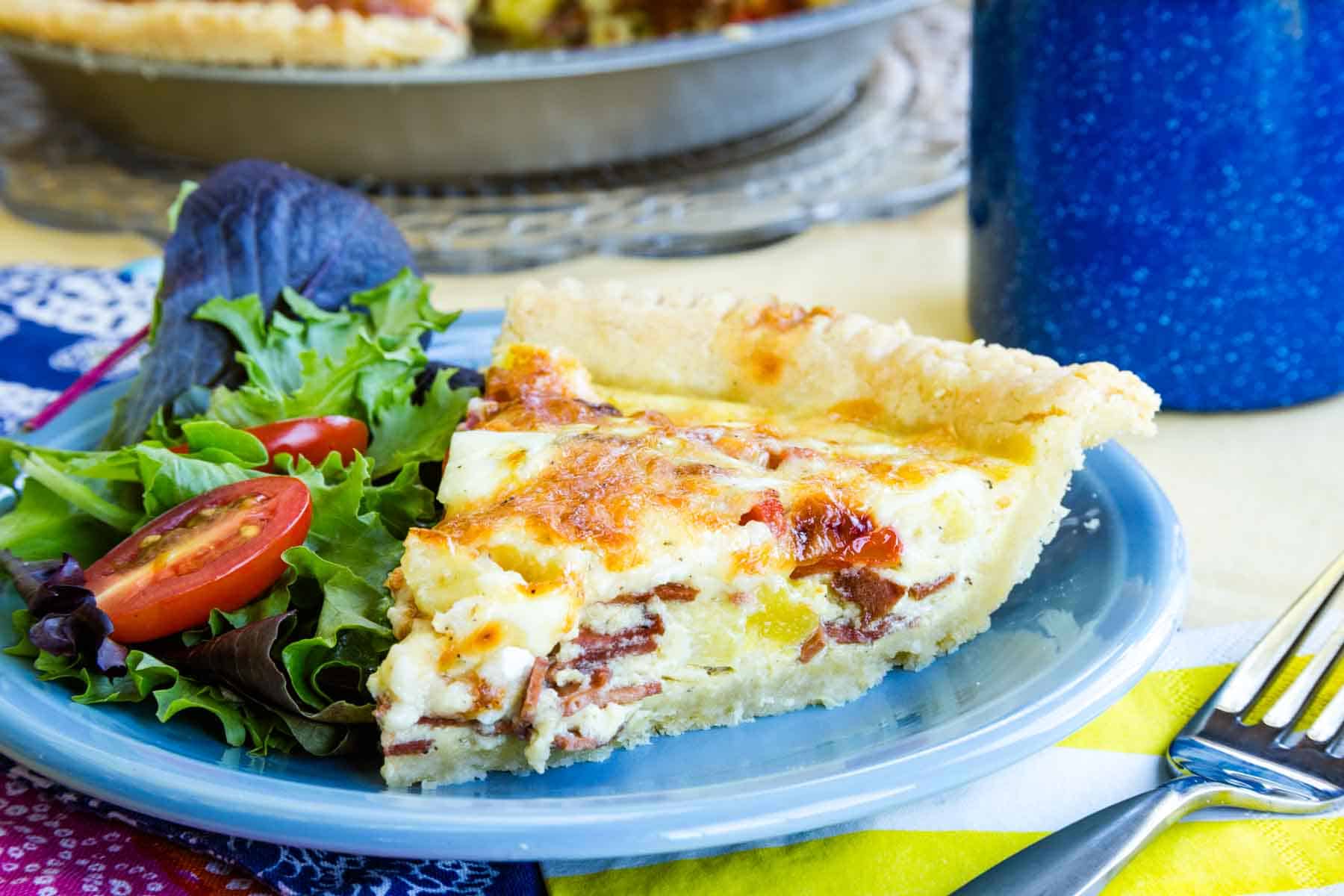 A slice of bacon cheddar quiche with salad on a plate
