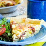 A slice of bacon cheddar quiche with a side salad on a plate, with the quiche in the background.