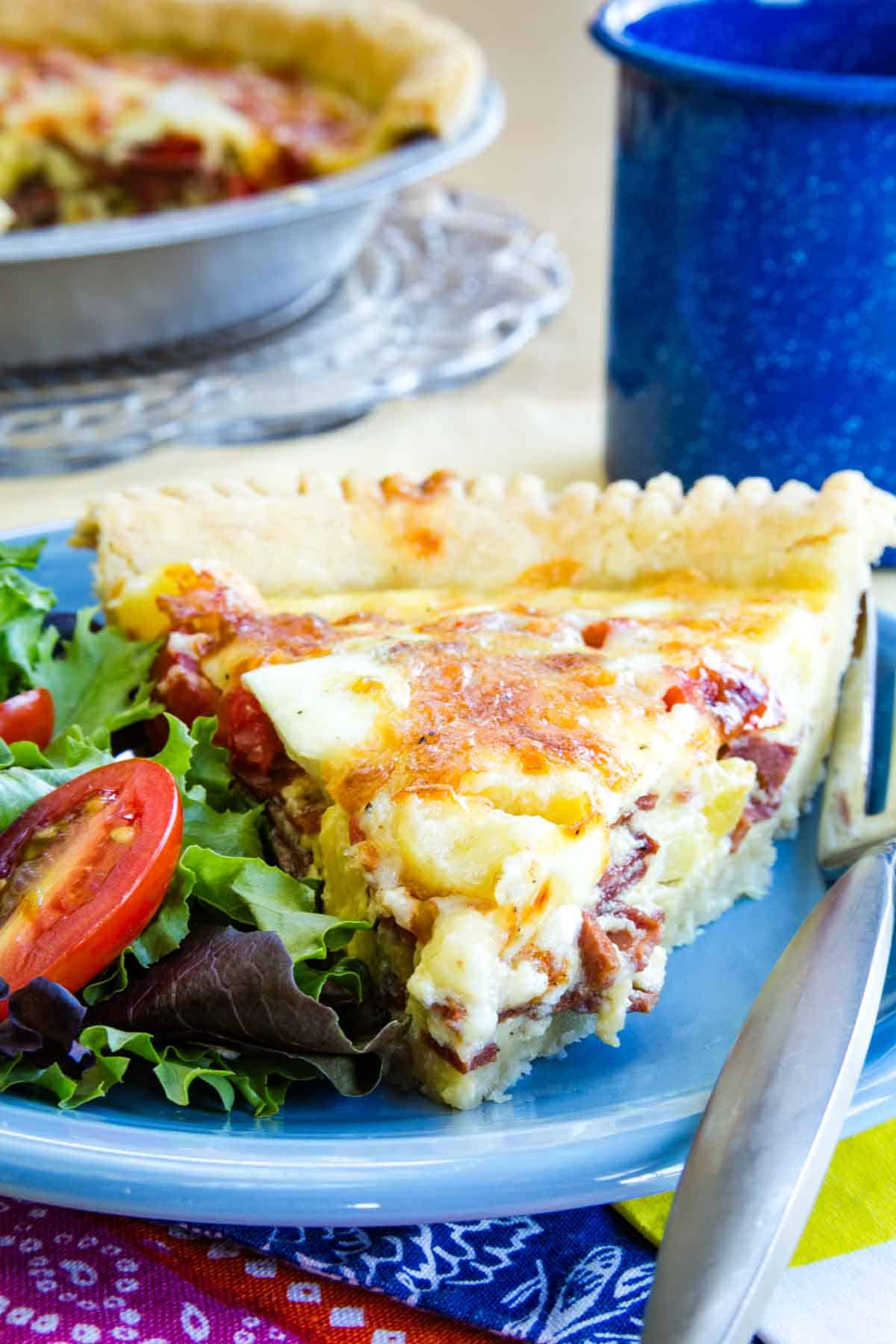 A piece of bacon cheddar quiche is served on a blue plate.