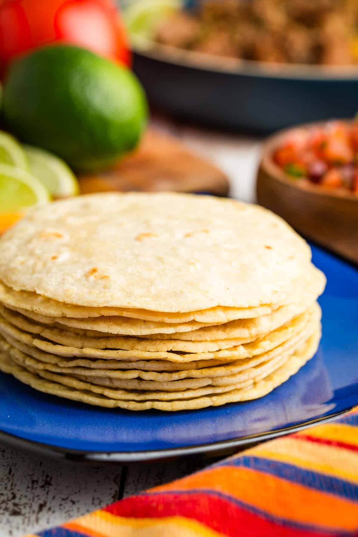 The easiest 4-ingredient corn tortillas recipe that makes perfect tortillas every time! Use these homemade beauties to make tacos and more. Corn tortillas are stacked up on a blue plate.