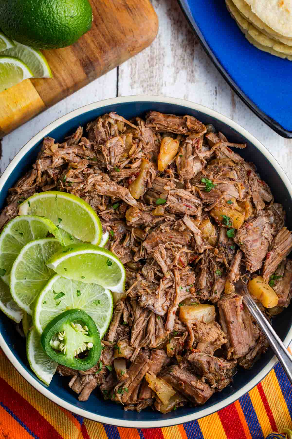 Crockpot barbacoa is a little sweet, a little spicy, and needs hardly any effort. Great in tacos, rice bowls, salads, and more. A spoon stirs a big bowl of crockpot barbacoa with lime slices.