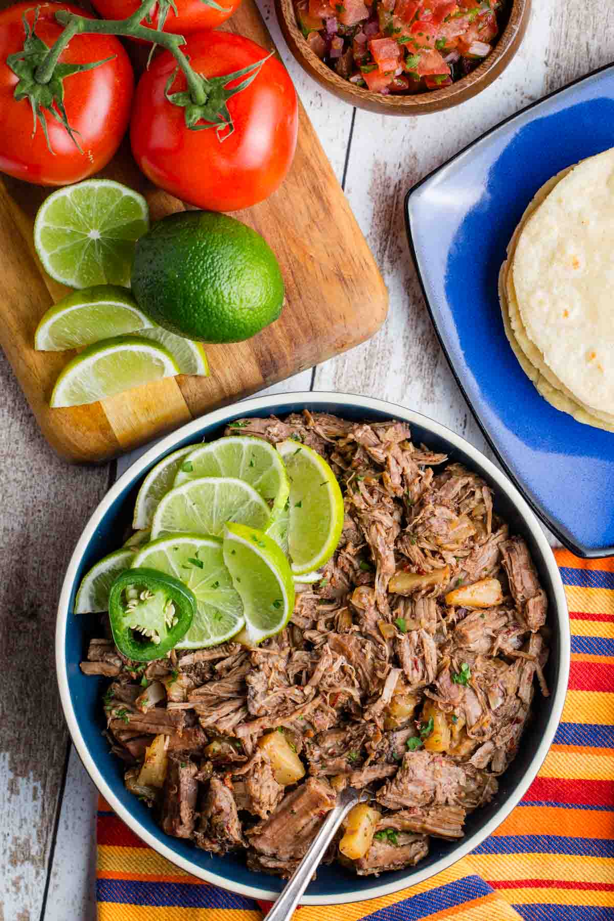 Sliced limes and peppers garnish a bowl of crockpot barbacoa.