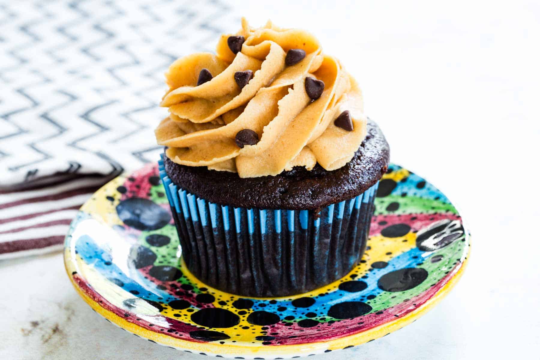 A chocolate cupcake with piped peanut butter frosting on a colorful plate.