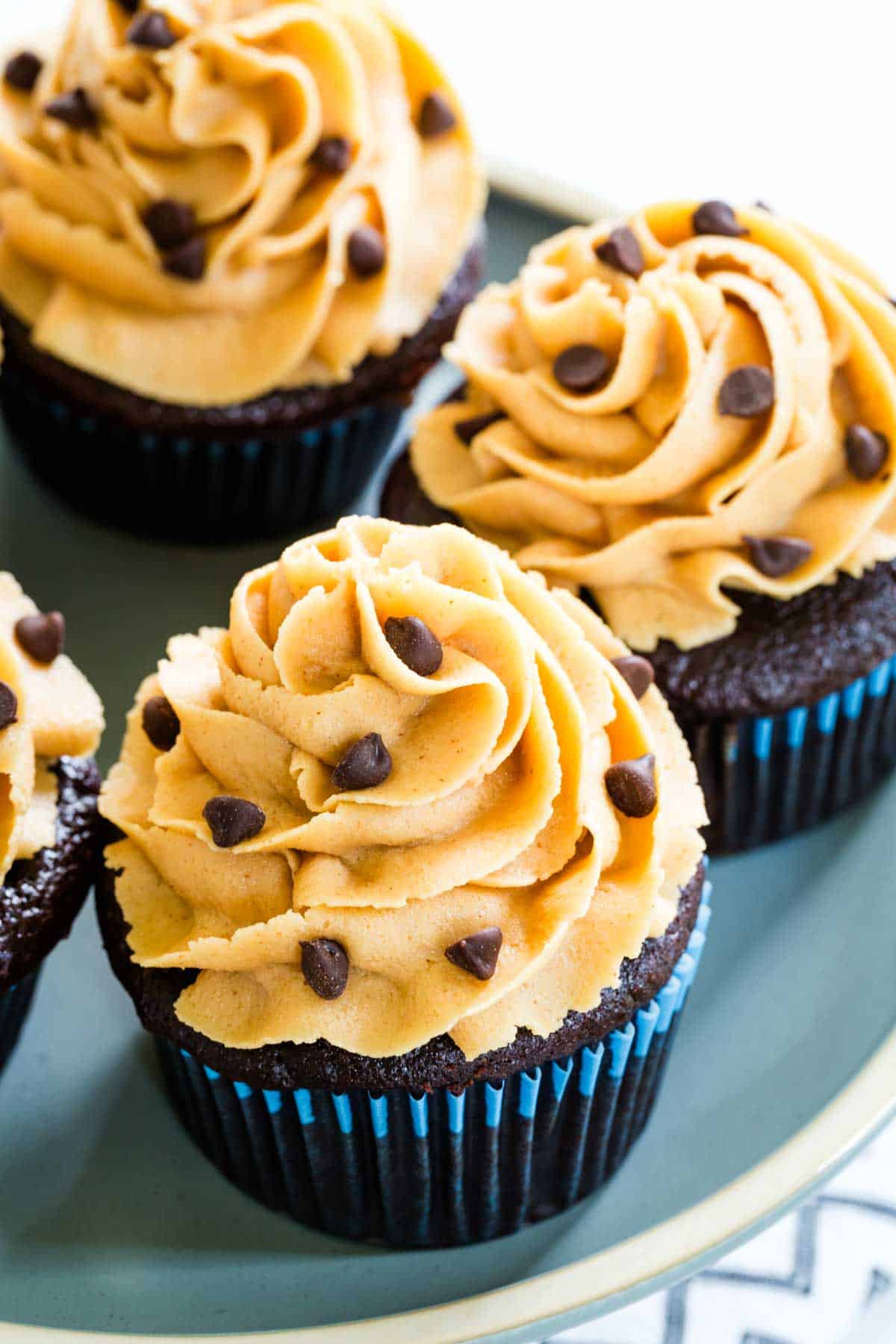 Chocolate cupcakes with a swirl of peanut butter frosting and mini chocolate chips on a blue plate.