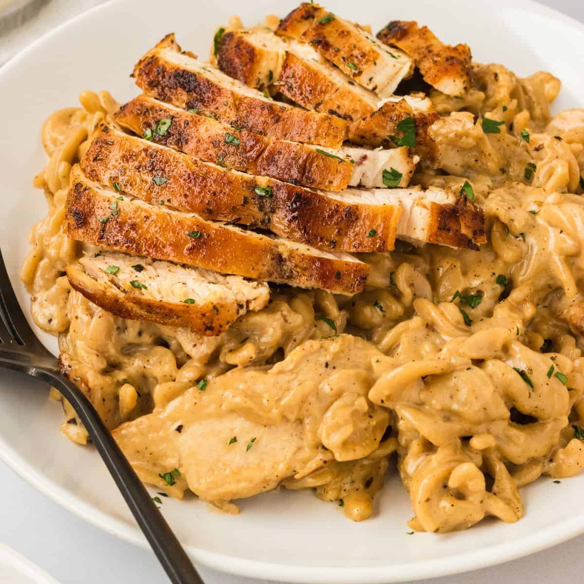 A plate of garlic parmesan chicken pasta with a fork.