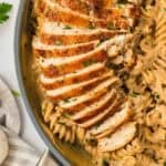 Slices of chicken are arranged on top of a pan of garlic parmesan chicken pasta.
