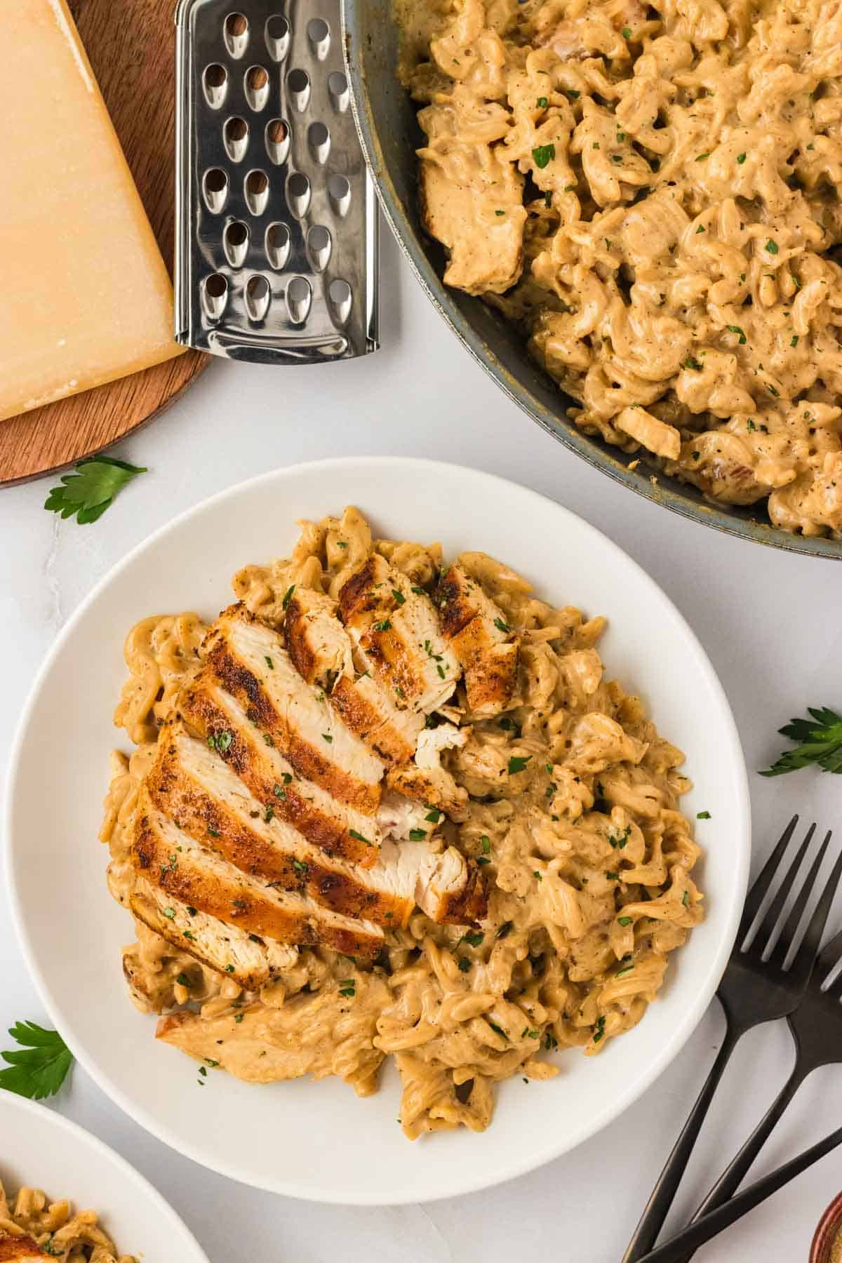 Garlic parmesan chicken pasta drapes tender chicken breasts in a rich and creamy sauce that's paired with gluten free pasta. A plate of garlic parmesan chicken pasta with a bowl of pasta next to it.