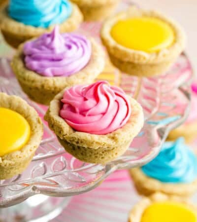 A cake stand holds sugar cookie cups filled with colored frosting.