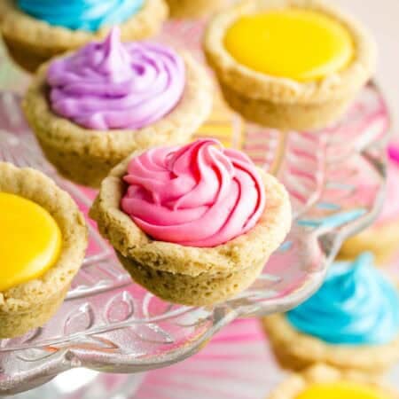 A cake stand holds sugar cookie cups filled with colored frosting.