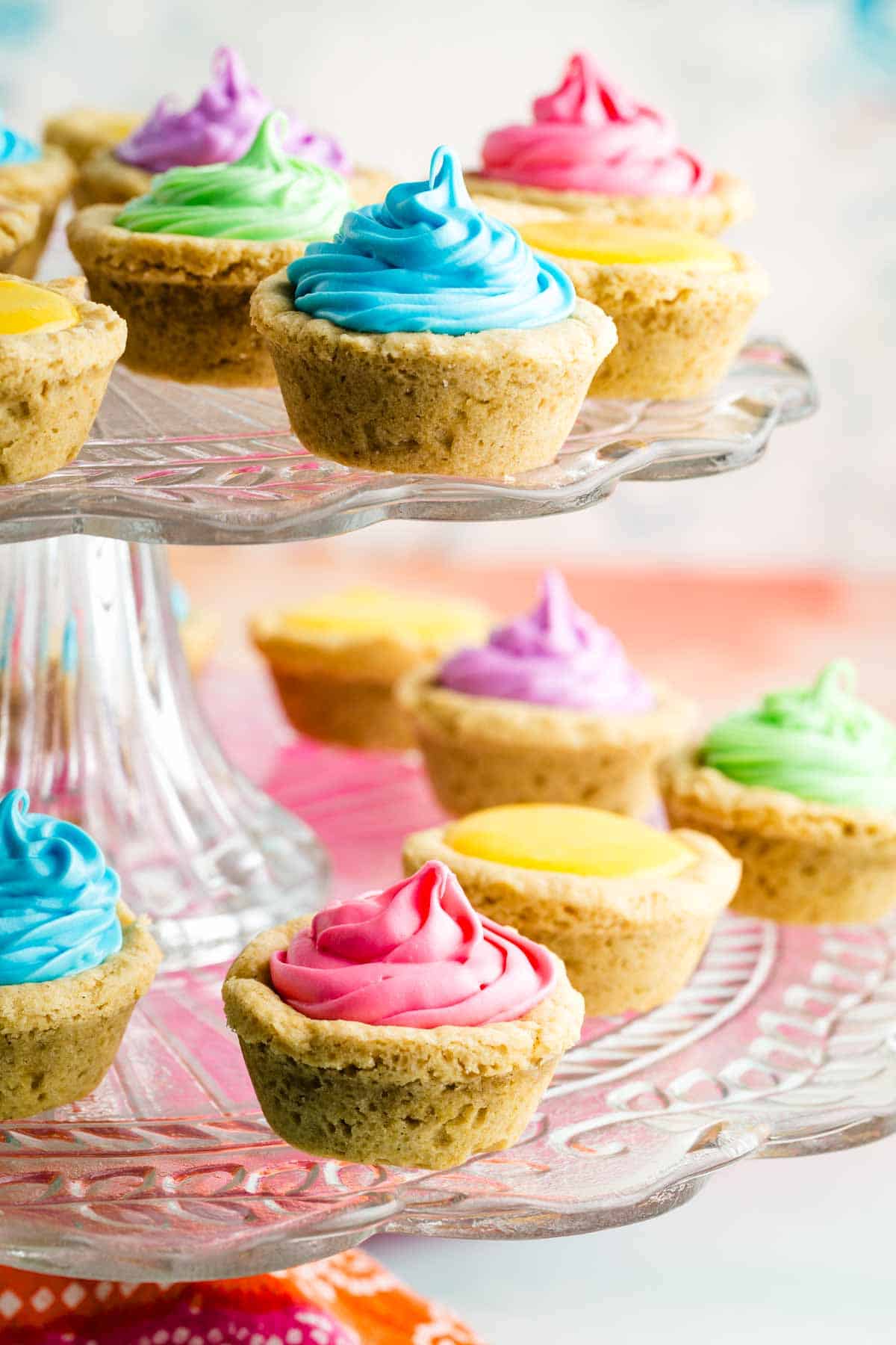 These cute gluten free sugar cookie cups can be filled with fluffy buttercream frosting, fruit curd, and more. Brightly colored buttercream fills sugar cookie cups.
