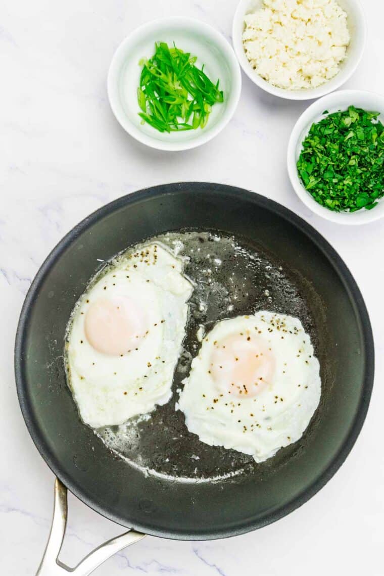 Fried eggs are flipped over to cook in a pan for breakfast tostadas.