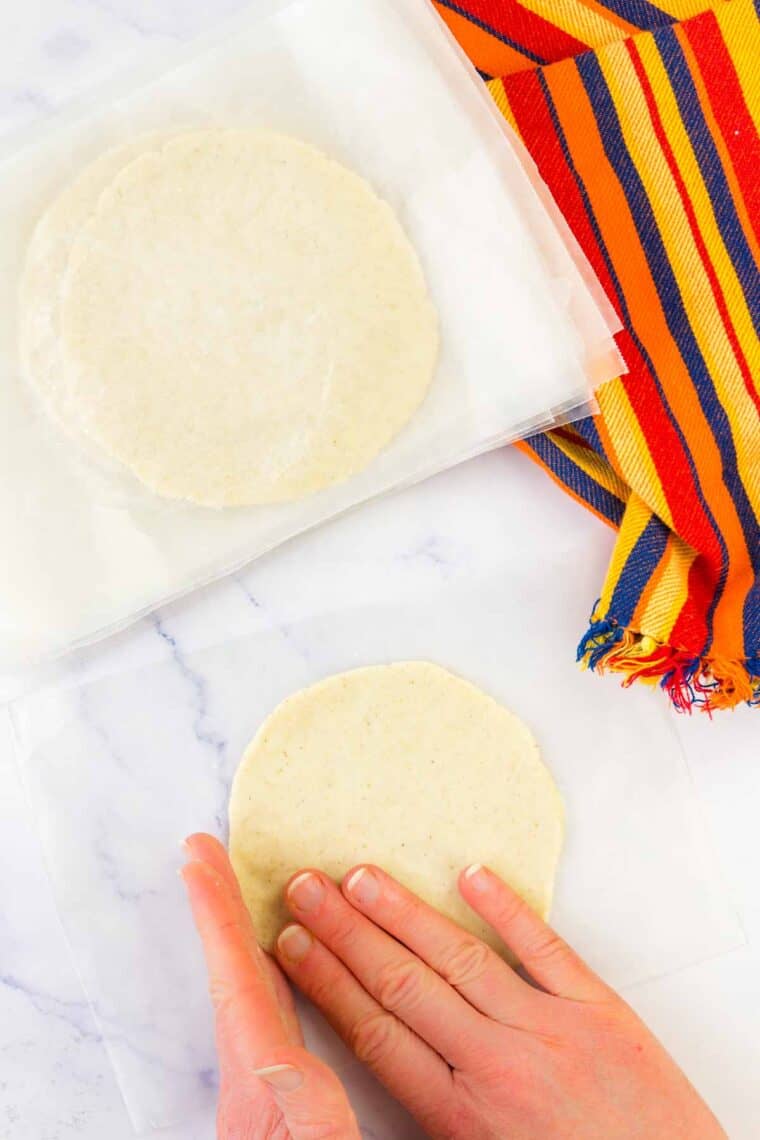 Hands smooth and press out corn tortillas dough.
