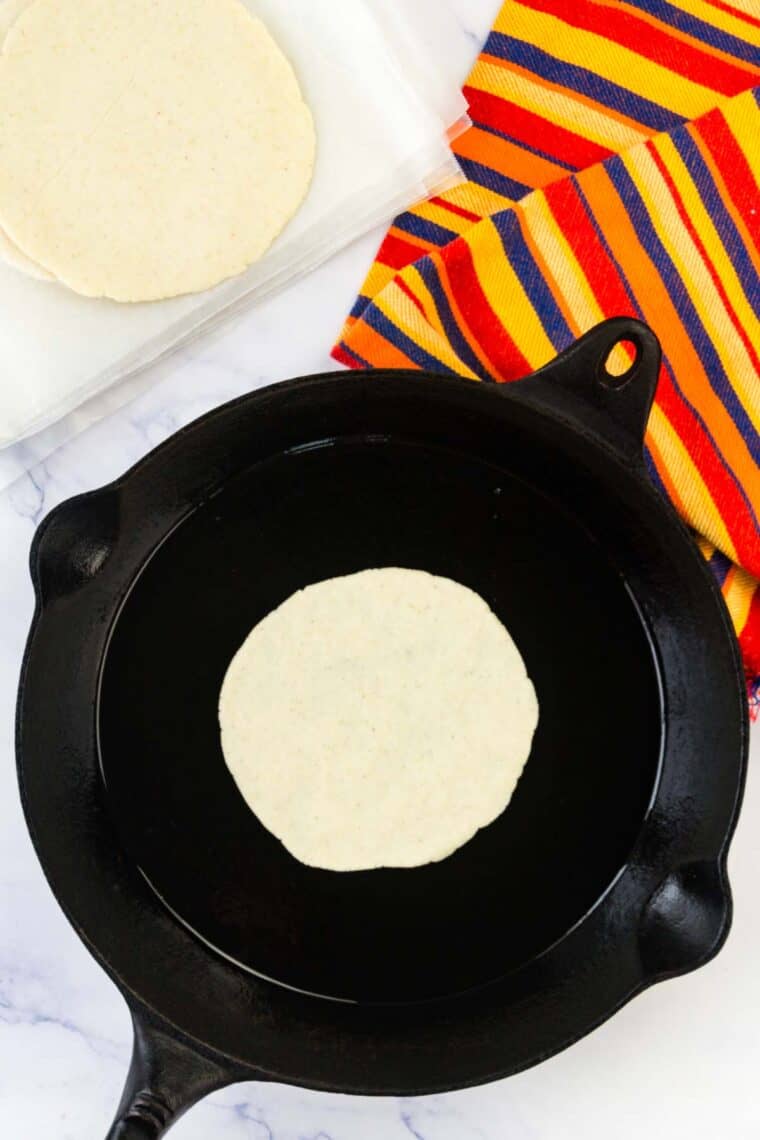 A corn tortilla cooks in a cast iron skillet.