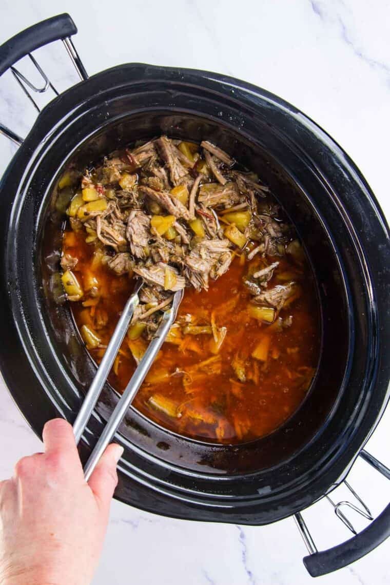 Tongs are used to stir a crockpot of barbacoa.