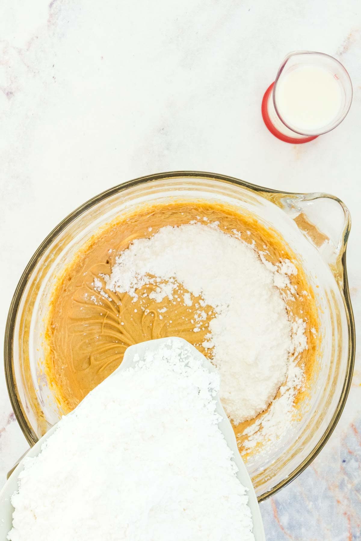 Powdered sugar being added to a bowl of creamed peanut butter and butter.