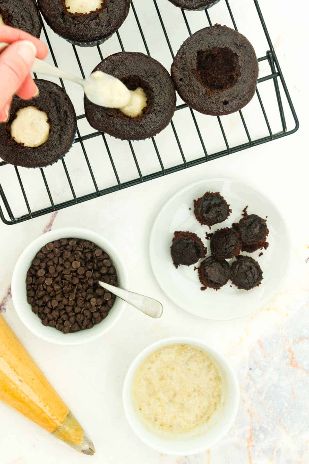 Banana filling being spooned into a hole in chocolate cupcakes.