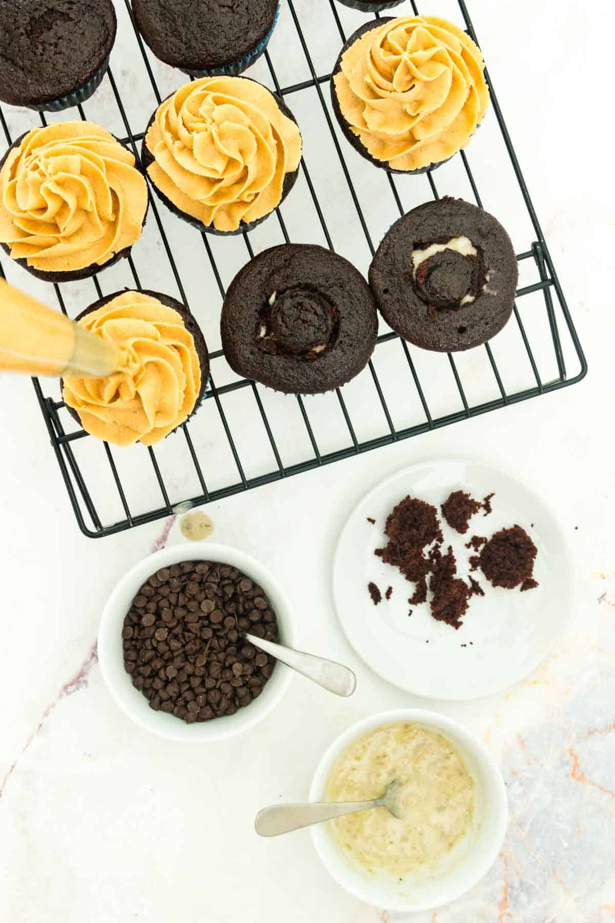 Peanut butter frosting being piped onto cupcakes on a rack.