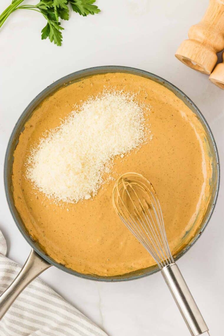 Garlic parmesan chicken pasta drapes tender chicken breasts in a rich and creamy sauce that's paired with gluten free pasta. Parmesan cheese is whisked into the sauce in a pan.
