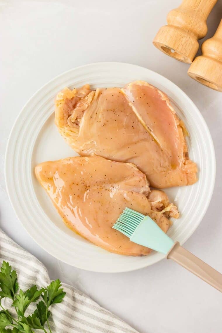 Garlic parmesan chicken pasta drapes tender chicken breasts in a rich and creamy sauce that's paired with gluten free pasta. A pastry brush is used to brush olive oil on 2 chicken breasts.