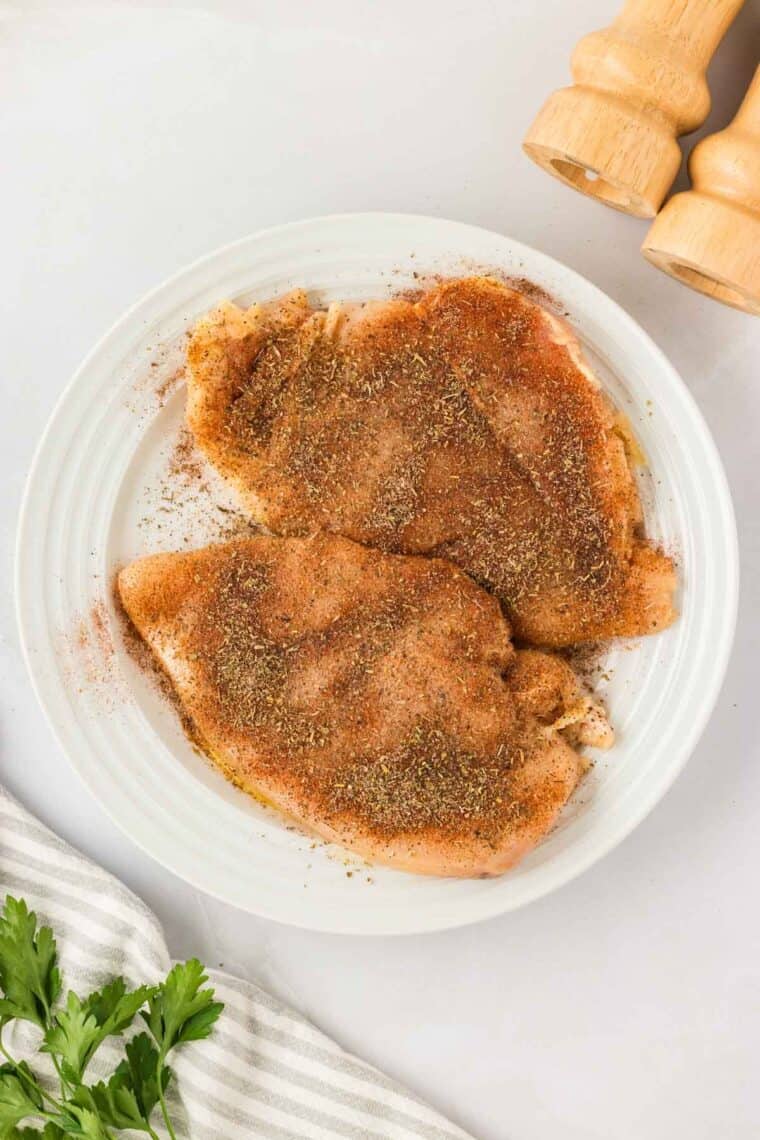Garlic parmesan chicken pasta drapes tender chicken breasts in a rich and creamy sauce that's paired with gluten free pasta. Two seasoned chicken breasts on a plate.