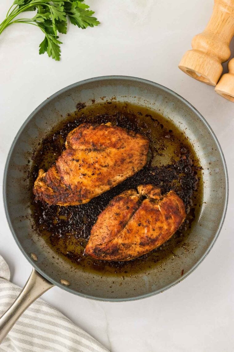 Garlic parmesan chicken pasta drapes tender chicken breasts in a rich and creamy sauce that's paired with gluten free pasta. Two chicken breasts brown in a pan.