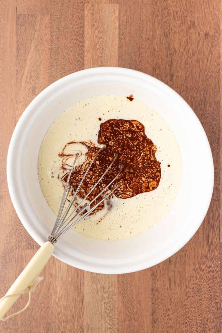 Melted chocolate is whisked into the wet ingredients in a bowl.
