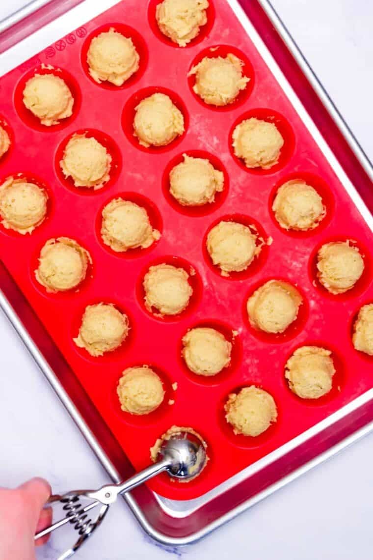 A cookie scoop adds sugar cookie cup dough to a baking pan.