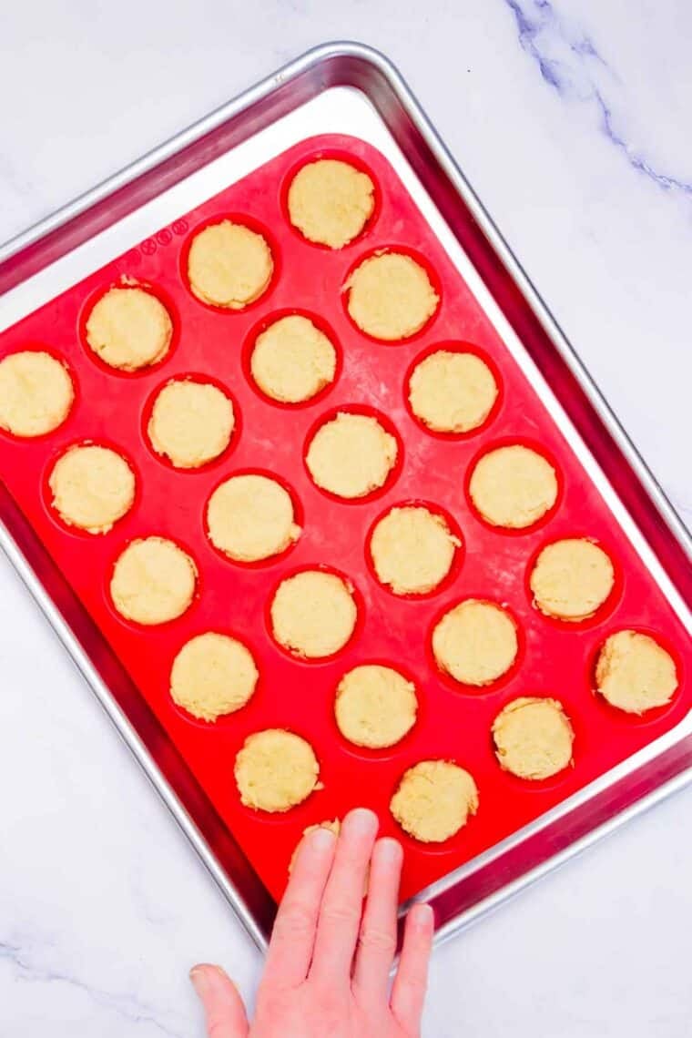 A hand pressing sugar cookie cups dough into a silicone baking pan.