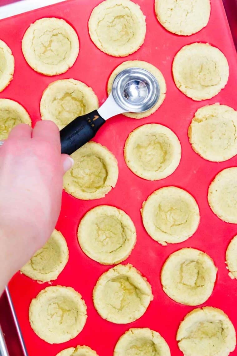 Using a spoon to press down sugar cookie cups dough in a baking pan.