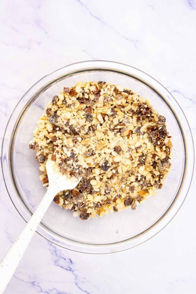 Oats and other ingredients for no bake granola bars are stirred together in a bowl.