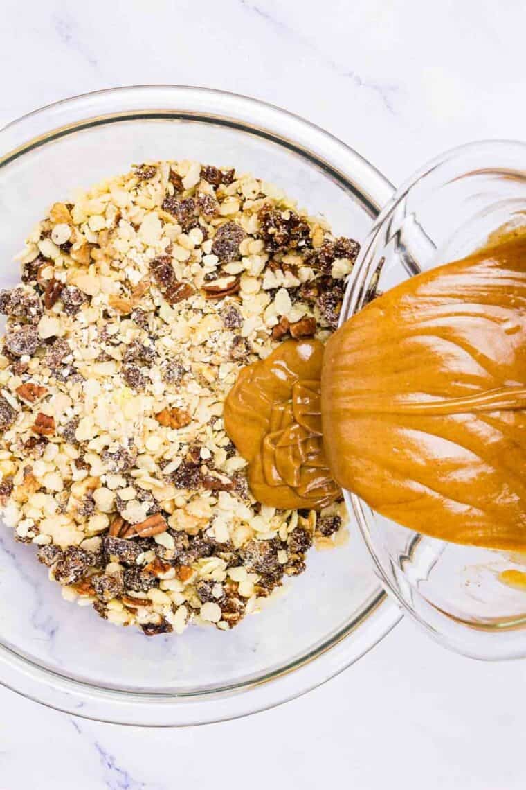 Melted peanut butter and honey is poured onto the dry mix for granola bars in a bowl.