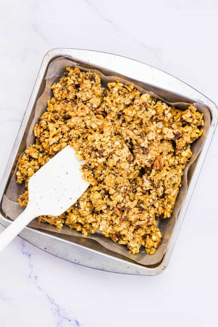 A spatula presses down no bake granola bar mixture into a pan.