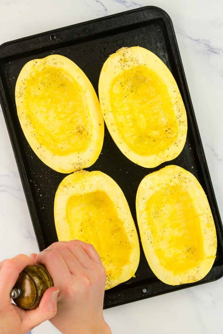 Spaghetti squash halves being seasoned on a baking sheet.