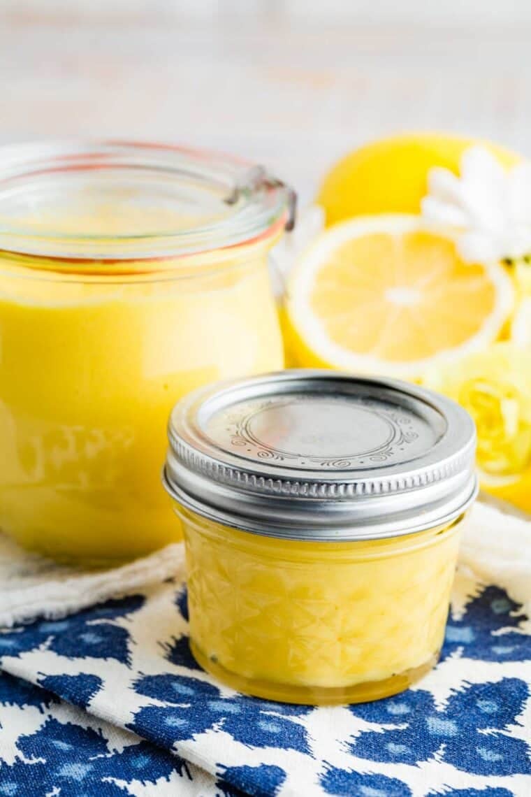 Jars full of lemon curd with halved lemons nearby.