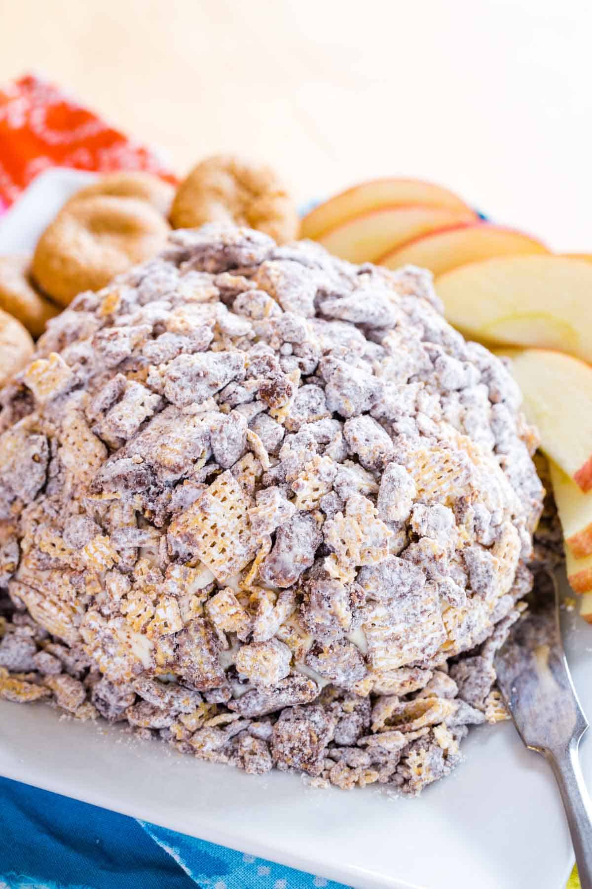 A platter with a dessert cheese ball covered with Muddy Buddies snack mix.