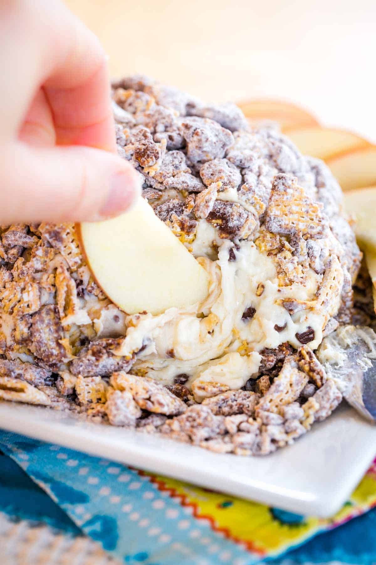 An apple slice scooping up some of the peanut butter chocolate chip cheese ball.