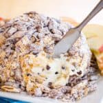 A dessert cheese ball coated with Muddy Buddies with a spreader knife in it with text overlay that says "Peanut Butter Chocolate Chip Cheese Ball".