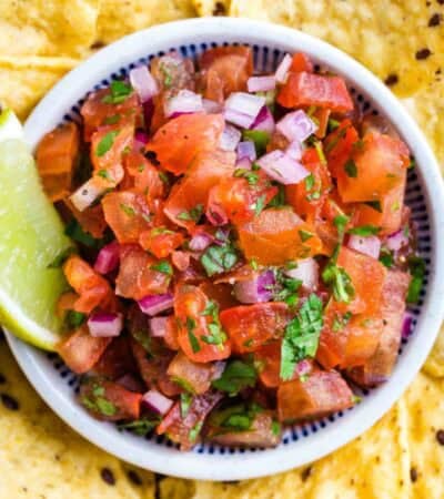 A lime wedge is inserted into a bowl of pico de gallo.