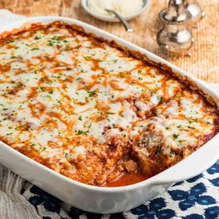 A white baking dish full of spaghetti squash lasagna with one portion removed.