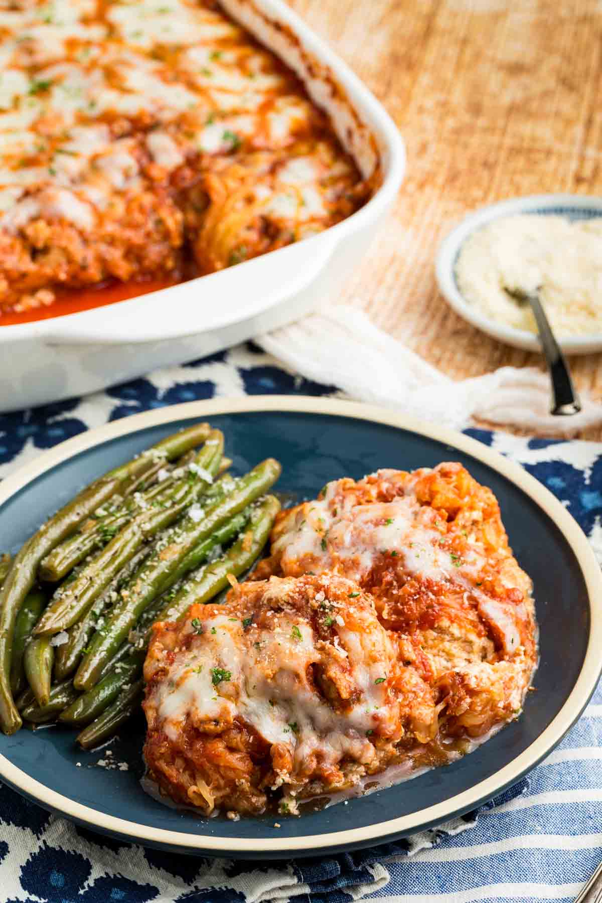 Spaghetti squash lasagna is loaded with turkey sausage, cheeses, and tender spaghetti squash. Naturally gluten-free! A plate of spaghetti squash lasagna with a side of vegetables and the pan of lasagna in the background.