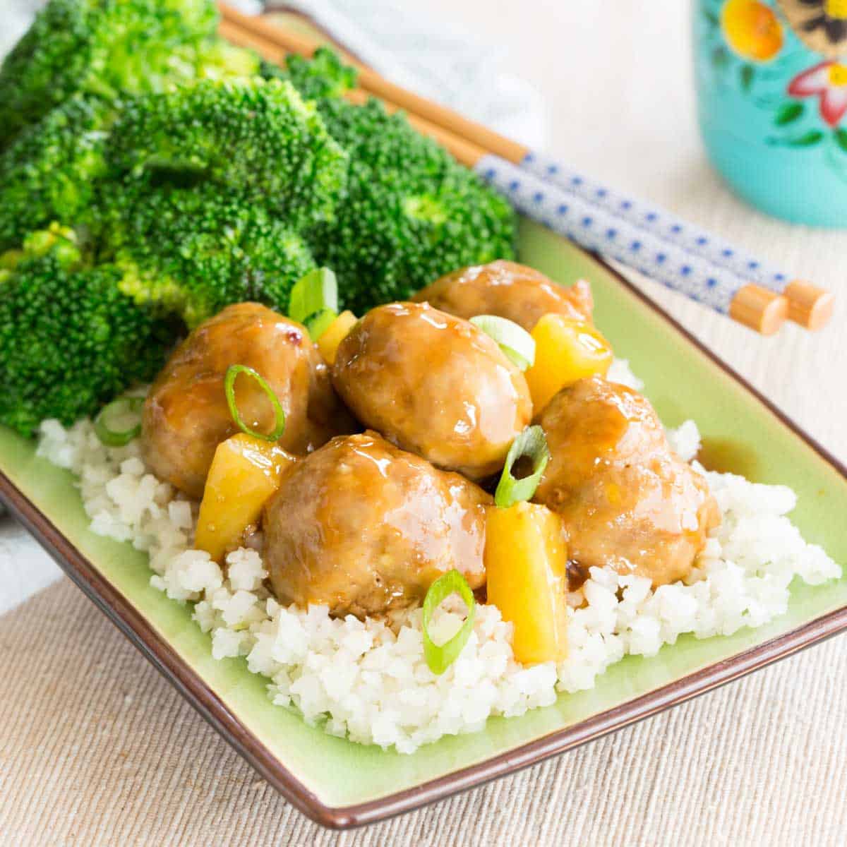 Teriyaki meatballs with pineapple, cauliflower rice, and broccoli on a green plate.